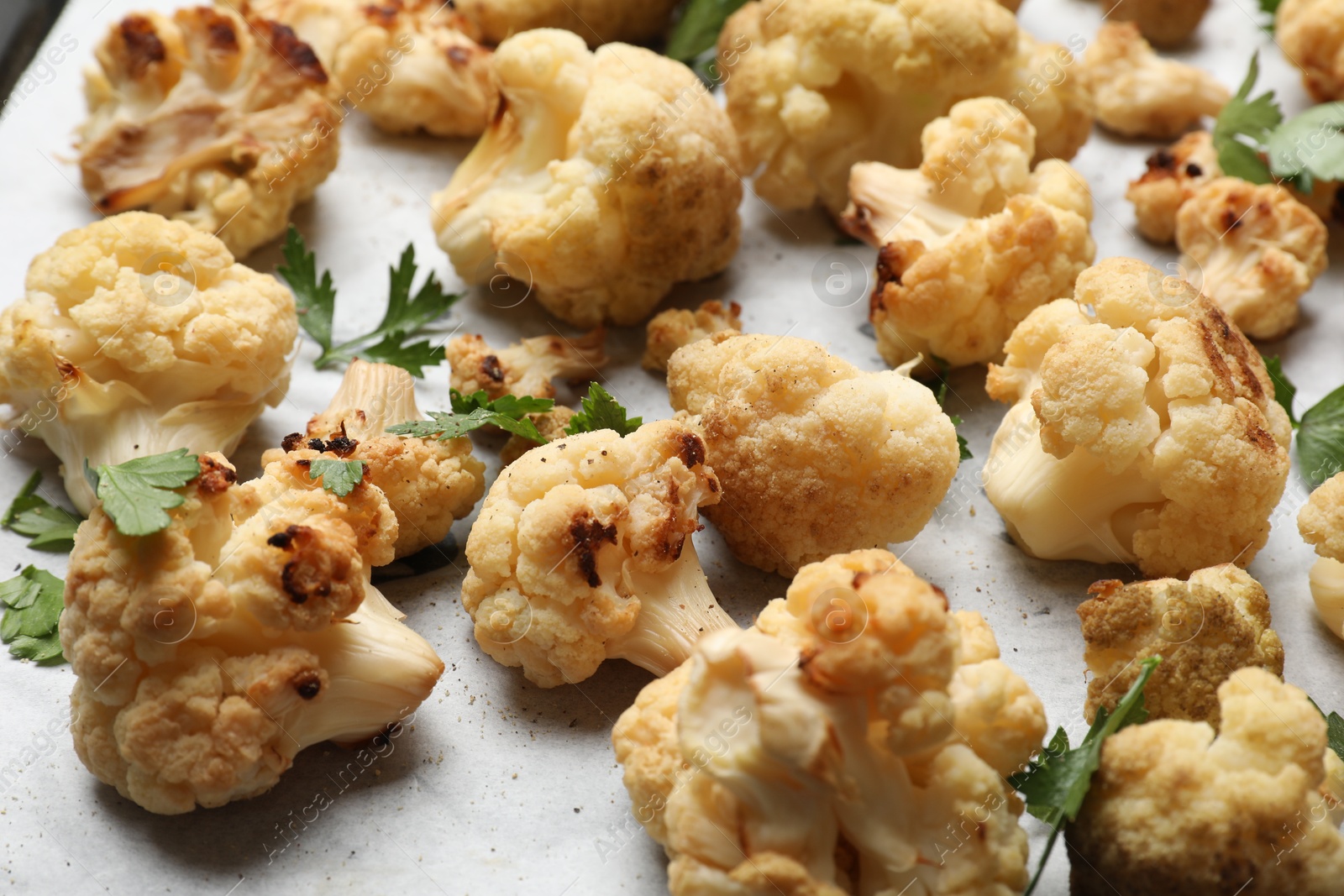 Photo of Tasty baked cauliflower and parsley on parchment, closeup