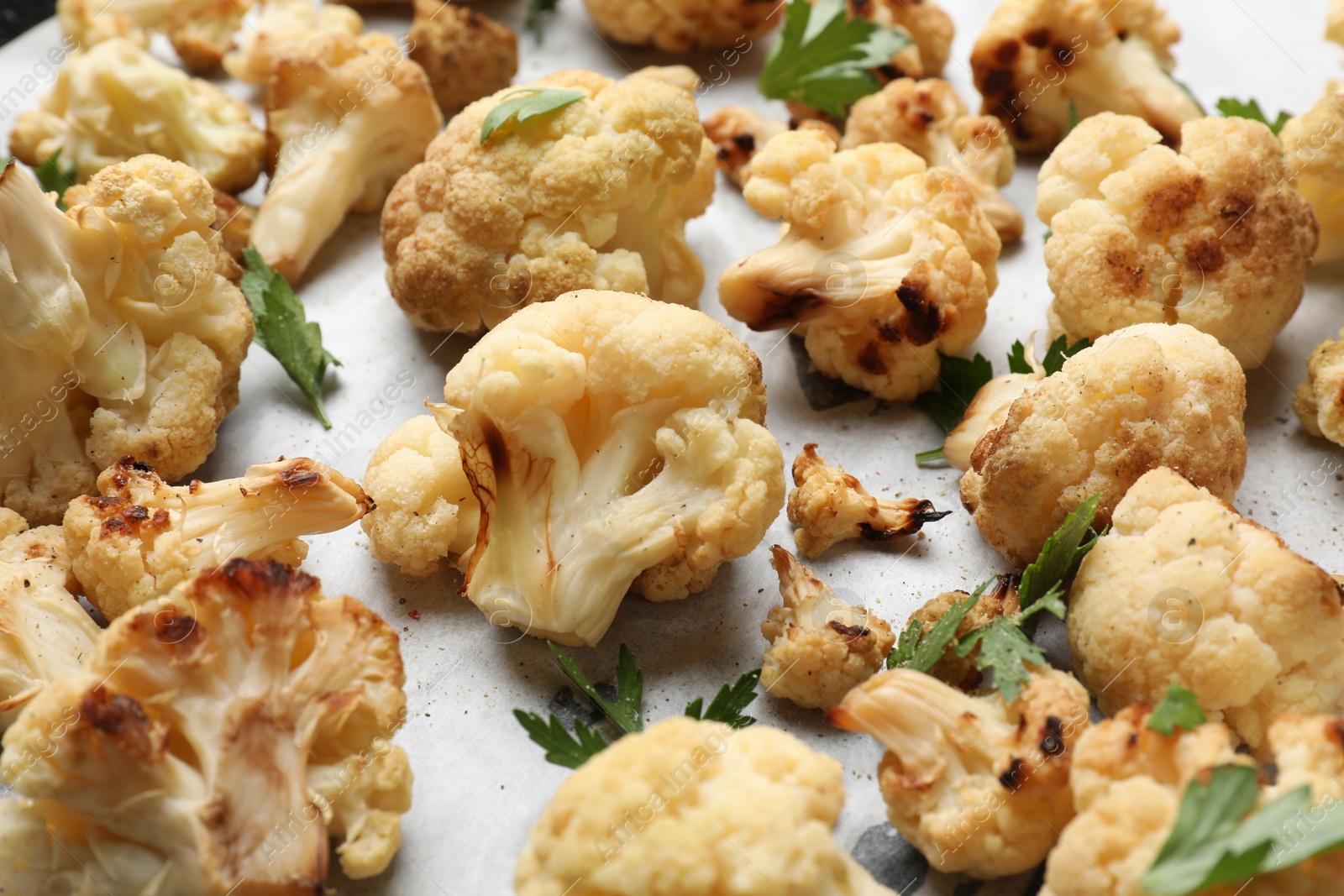 Photo of Tasty baked cauliflower and parsley on parchment, closeup