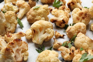 Tasty baked cauliflower and parsley on parchment, closeup