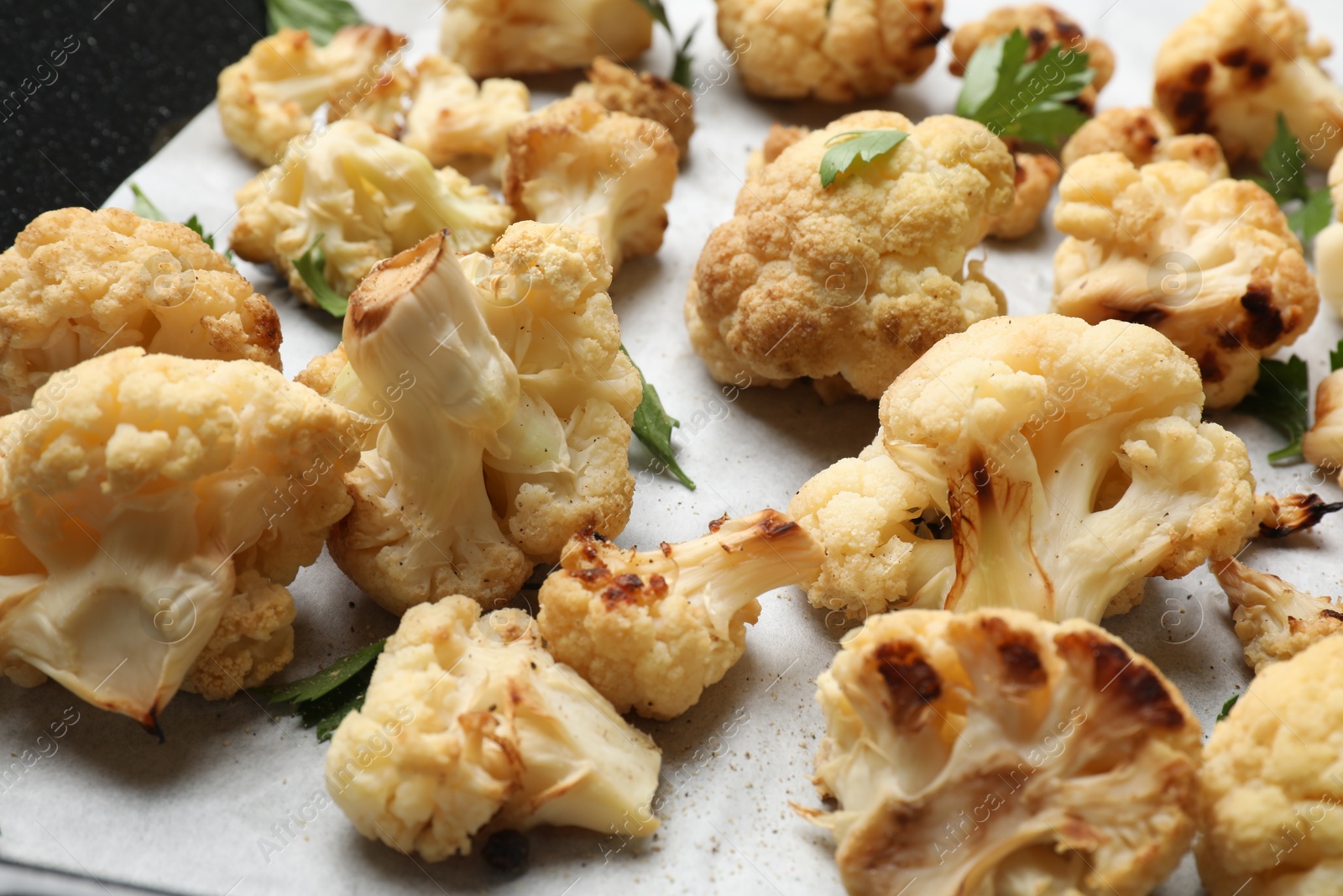 Photo of Tasty baked cauliflower and parsley on parchment, closeup