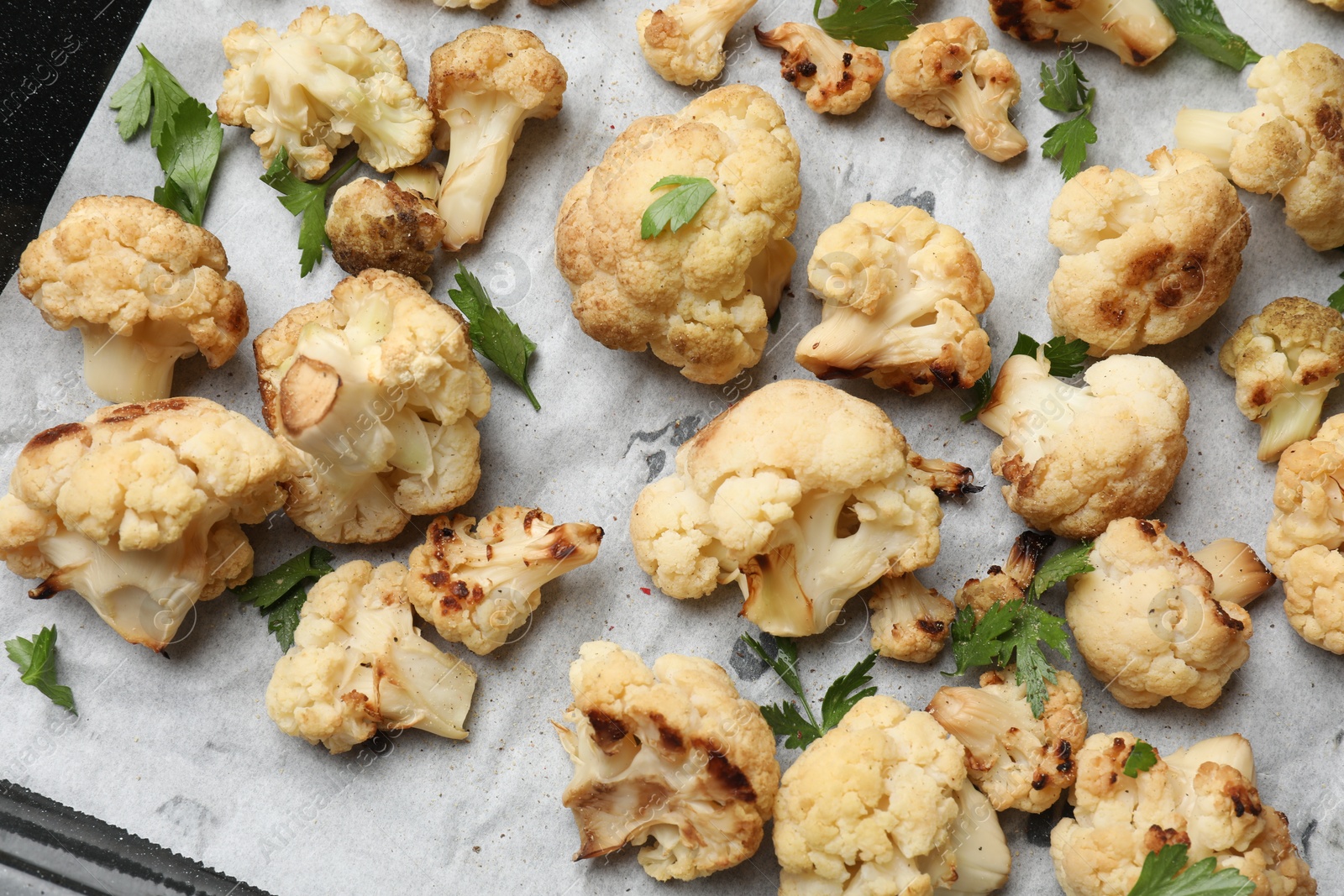 Photo of Tasty baked cauliflower and parsley on baking tray, top view