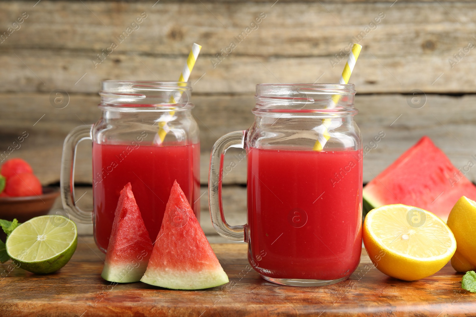 Photo of Tasty watermelon drink in mason jars and fresh fruits on wooden table, closeup