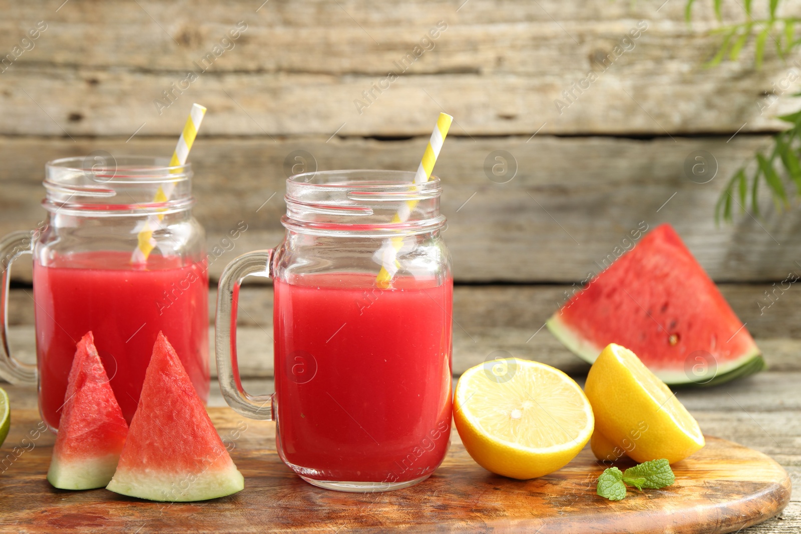 Photo of Tasty watermelon drink in mason jars and fresh fruits on wooden table, closeup