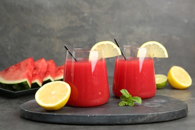 Photo of Delicious watermelon drink in glasses, fresh fruits and mint on grey table