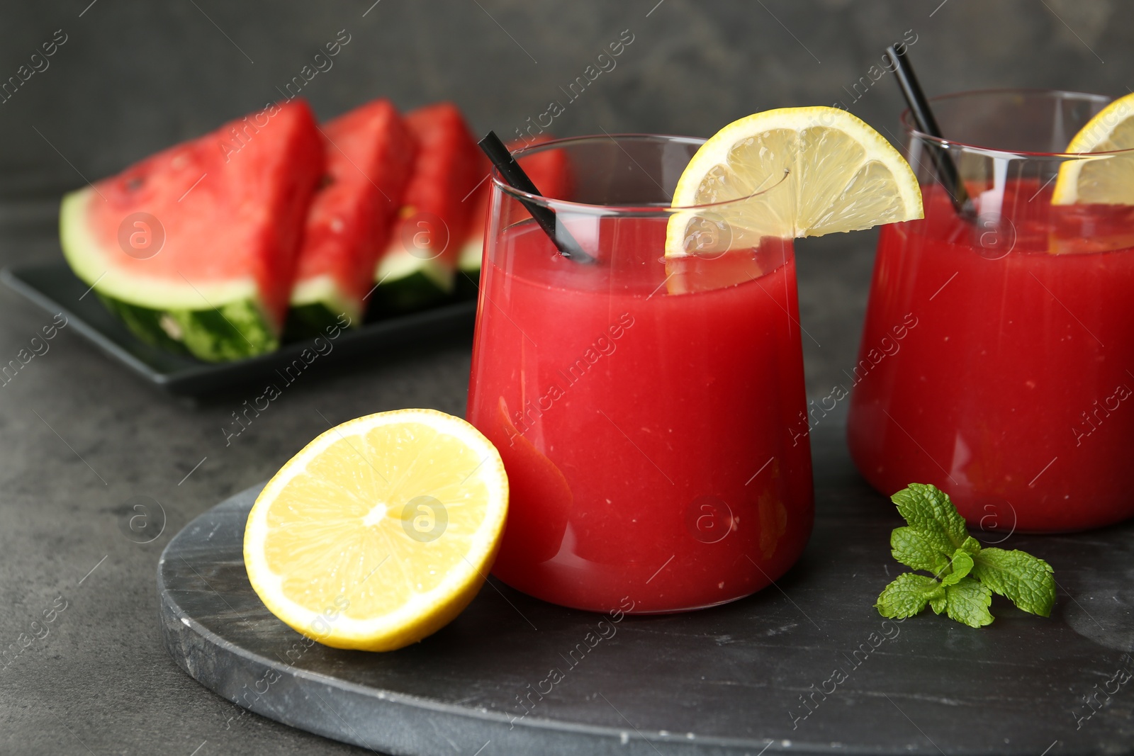 Photo of Delicious watermelon drink in glasses, fresh fruits and mint on grey table, closeup