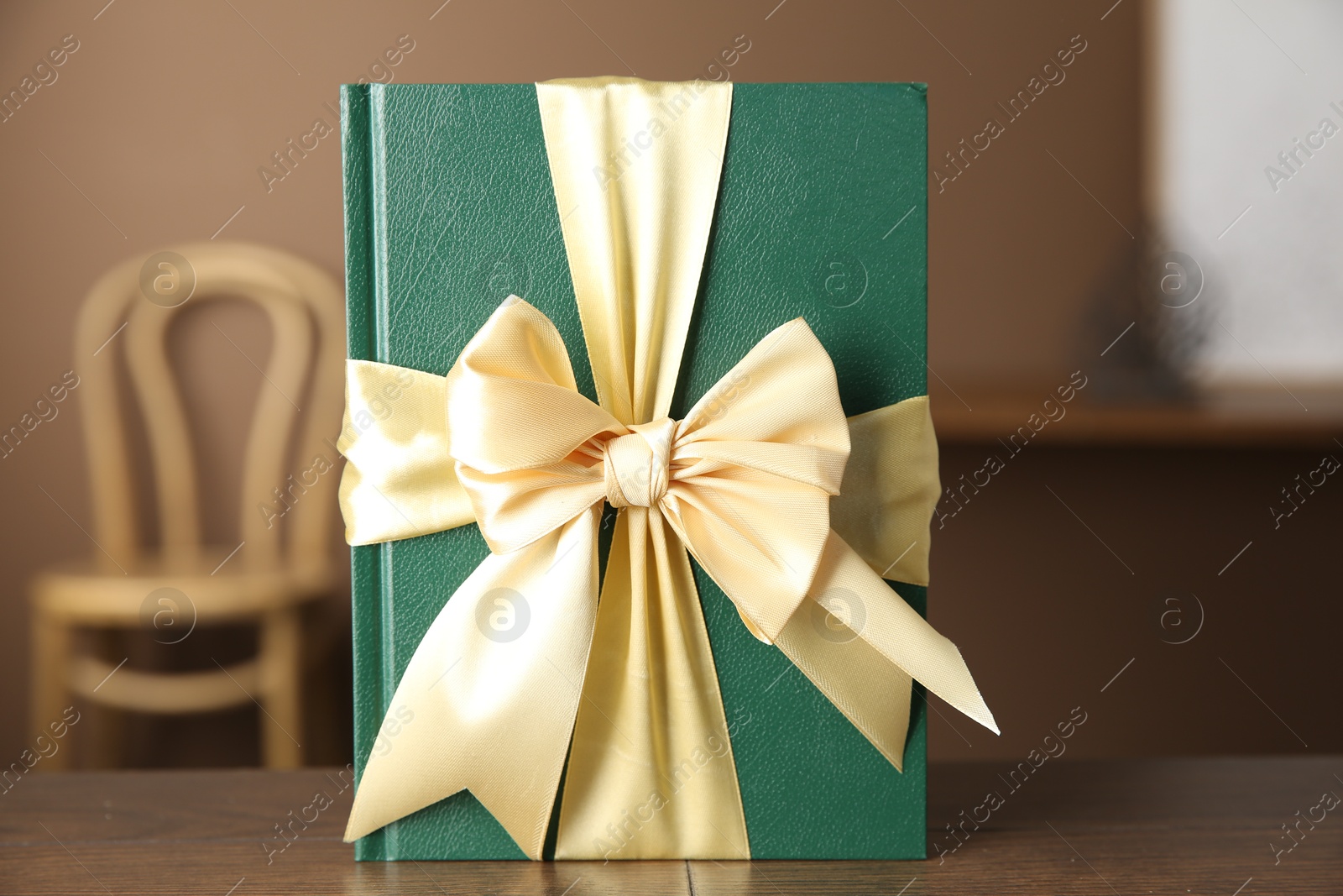 Photo of One book tied with ribbon as gift on wooden table indoors, closeup