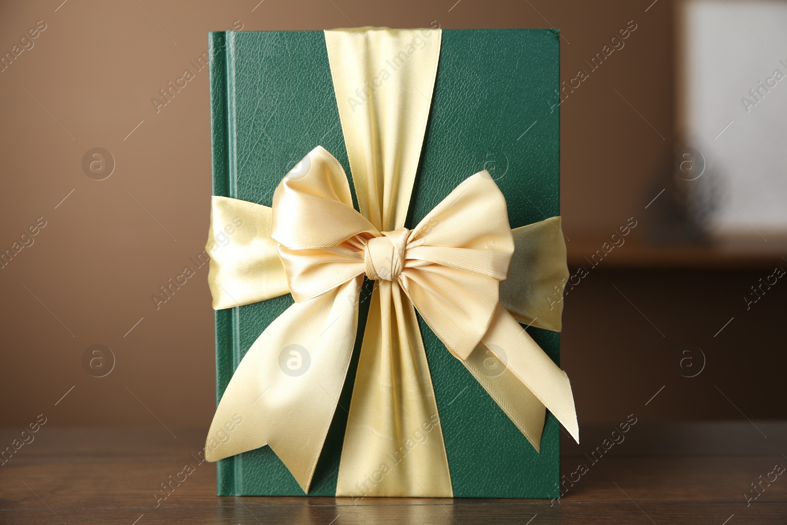 Photo of One book tied with ribbon as gift on wooden table indoors, closeup