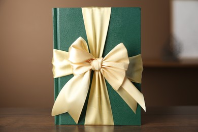 Photo of One book tied with ribbon as gift on wooden table indoors, closeup