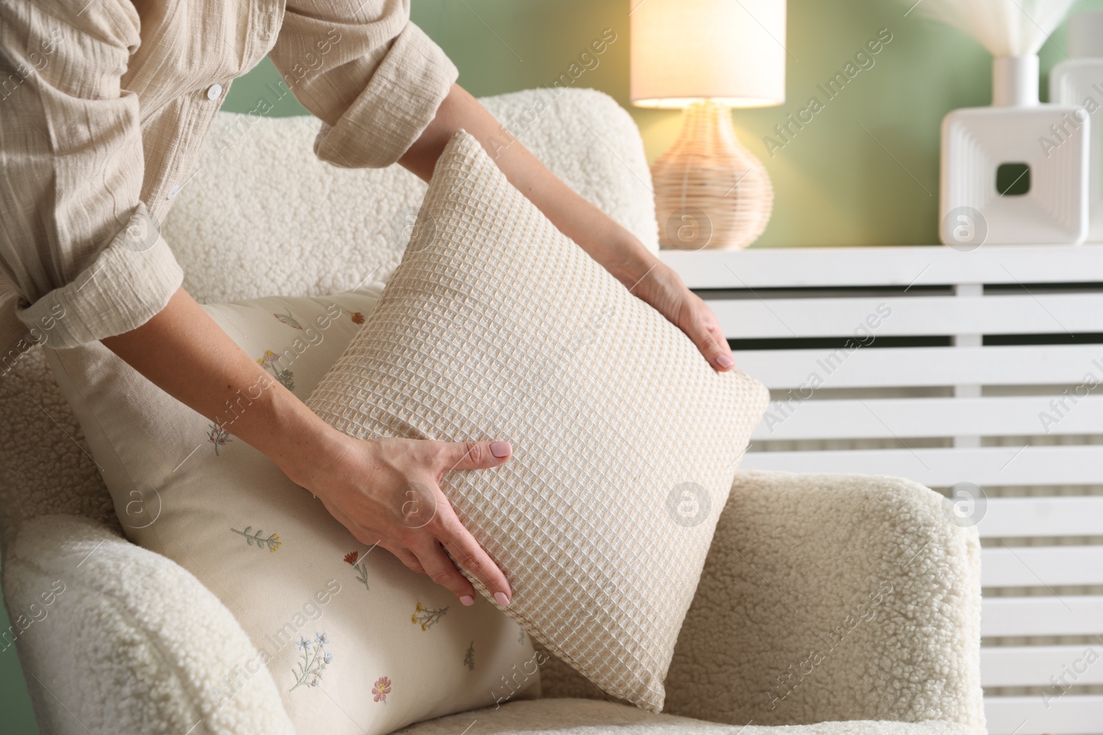 Photo of Woman putting soft pillow onto light armchair in living room, closeup