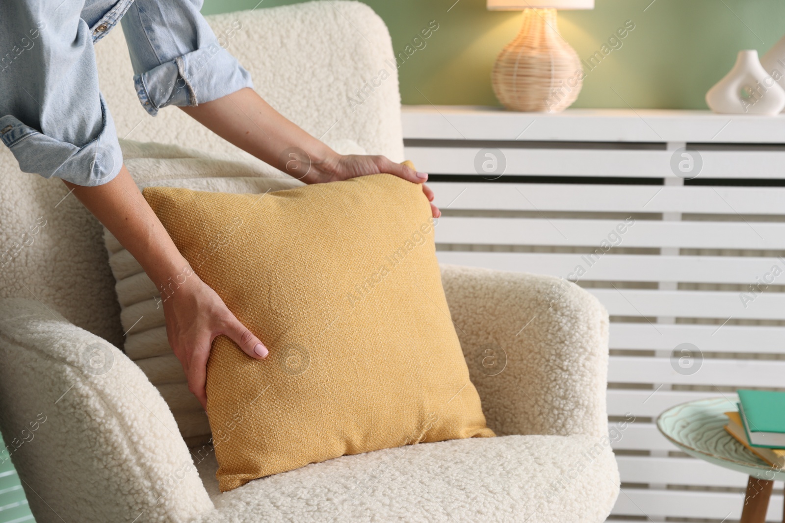 Photo of Woman putting soft pillow onto light armchair in living room, closeup