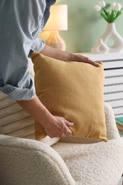 Photo of Woman putting soft pillow onto light armchair in living room, closeup