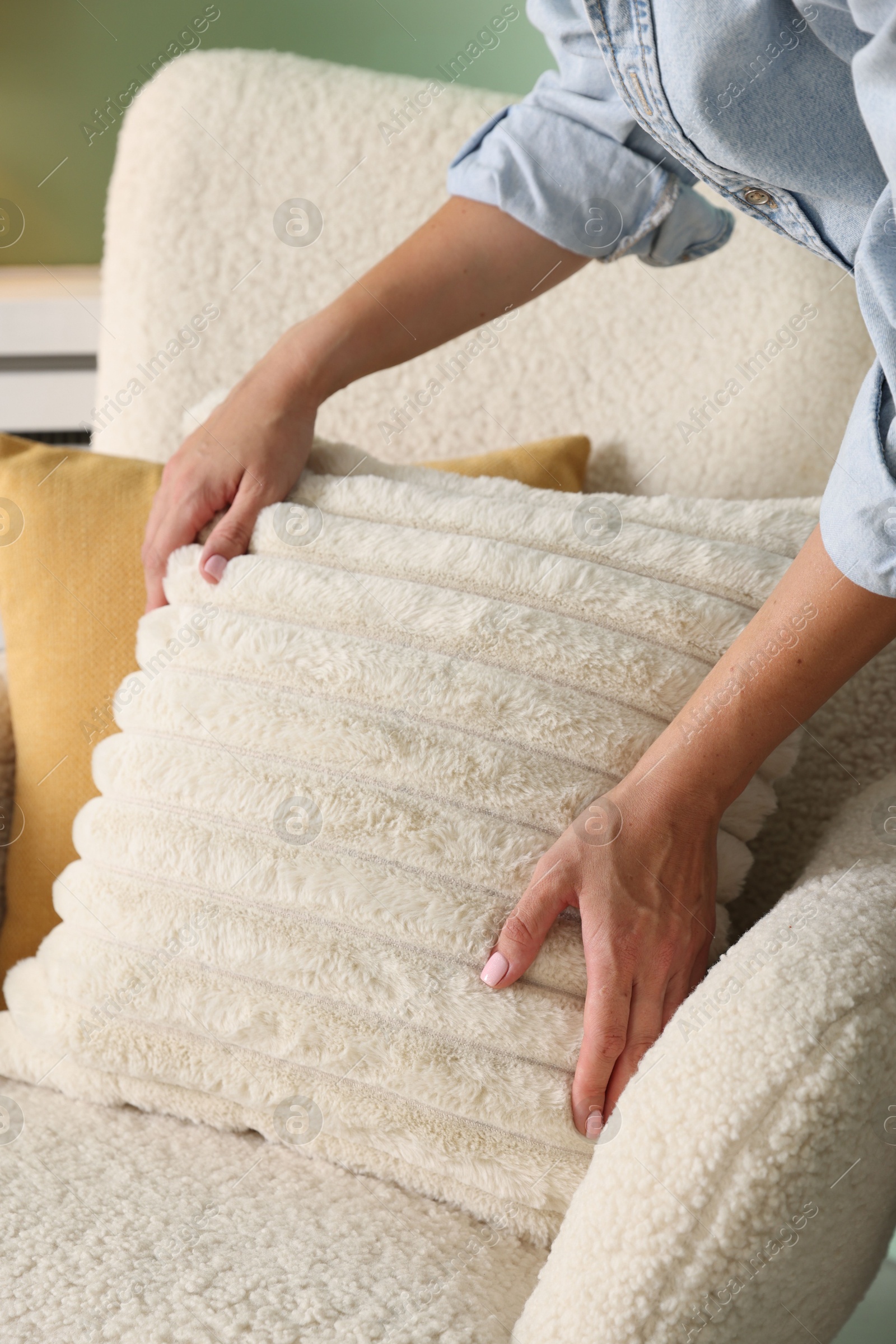 Photo of Woman putting soft pillow onto light armchair in living room, closeup