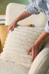 Woman putting soft pillow onto light armchair in living room, closeup