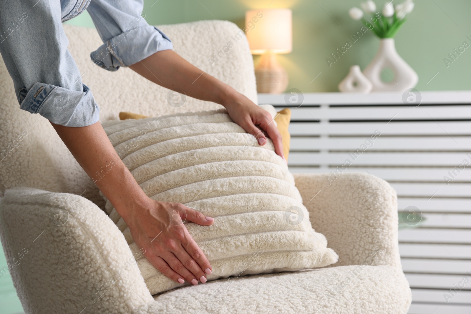 Photo of Woman putting soft pillow onto light armchair in living room, closeup