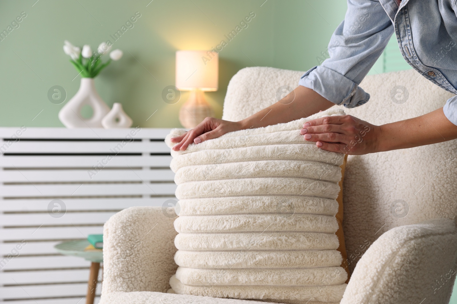 Photo of Woman putting soft pillow onto light armchair in living room, closeup