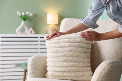 Photo of Woman putting soft pillow onto light armchair in living room, closeup