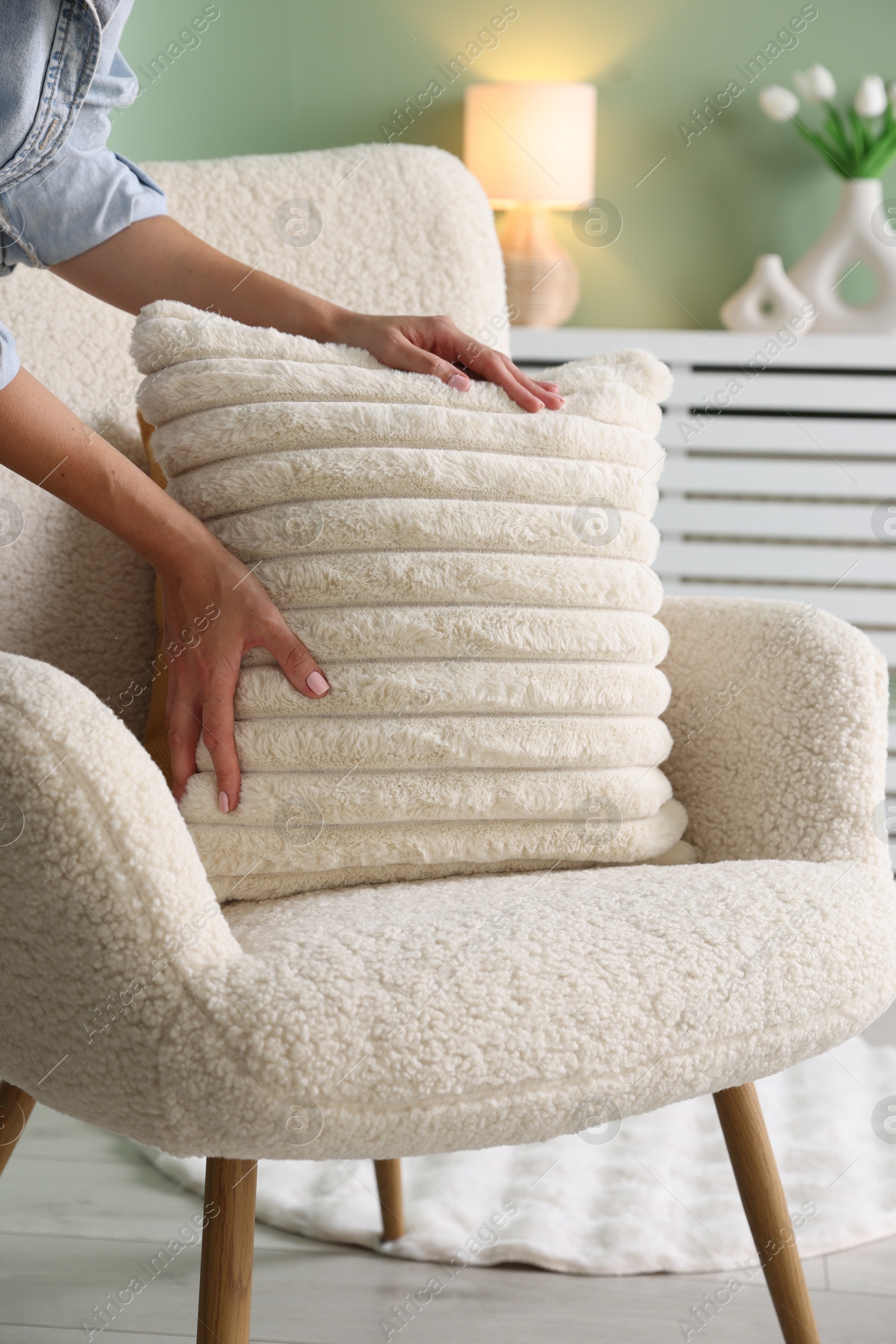 Photo of Woman putting soft pillow onto light armchair in living room, closeup