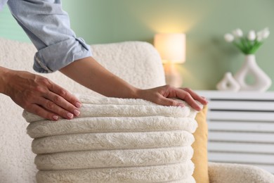 Photo of Woman putting soft pillow onto light armchair in living room, closeup