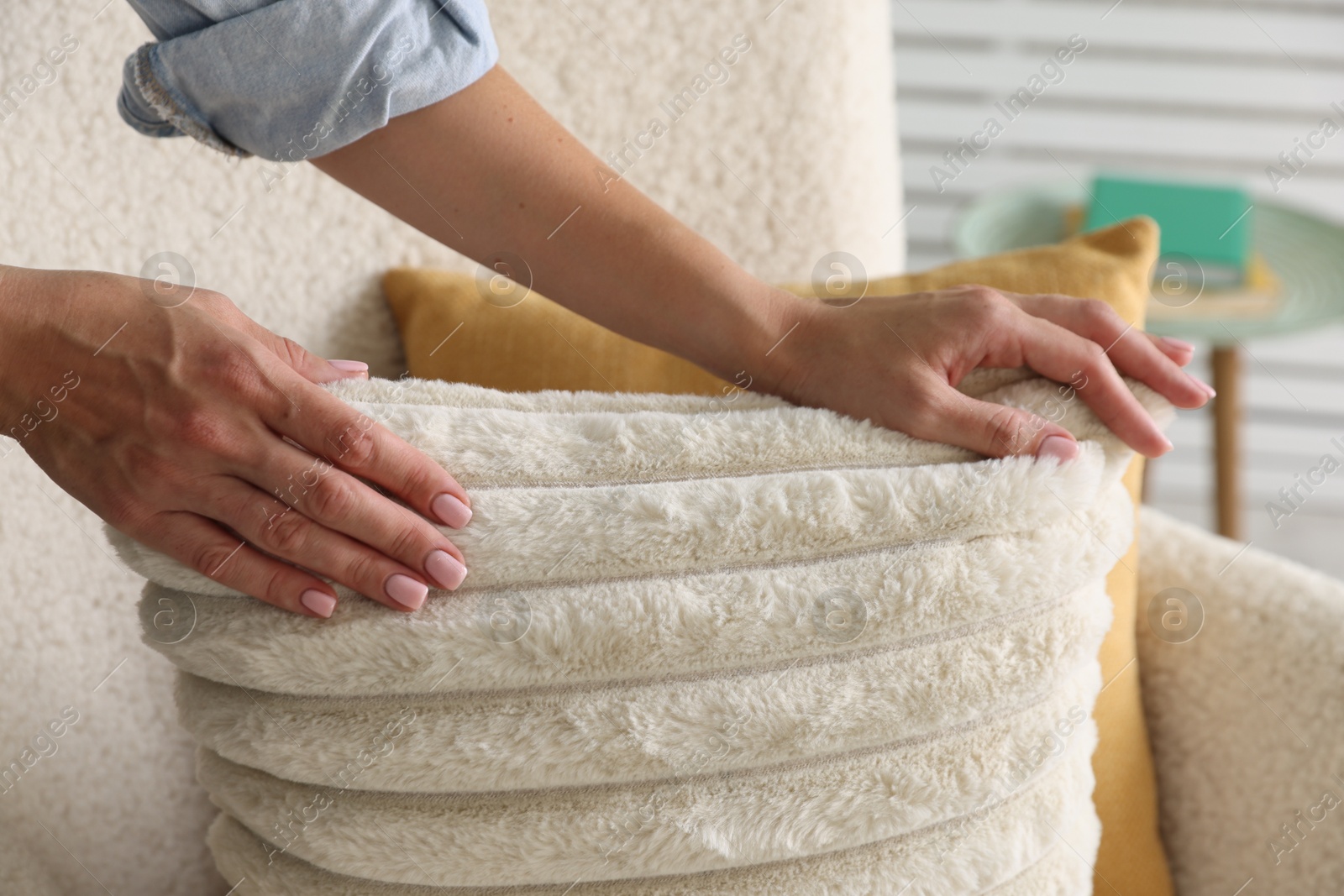 Photo of Woman putting soft pillow onto light armchair in living room, closeup