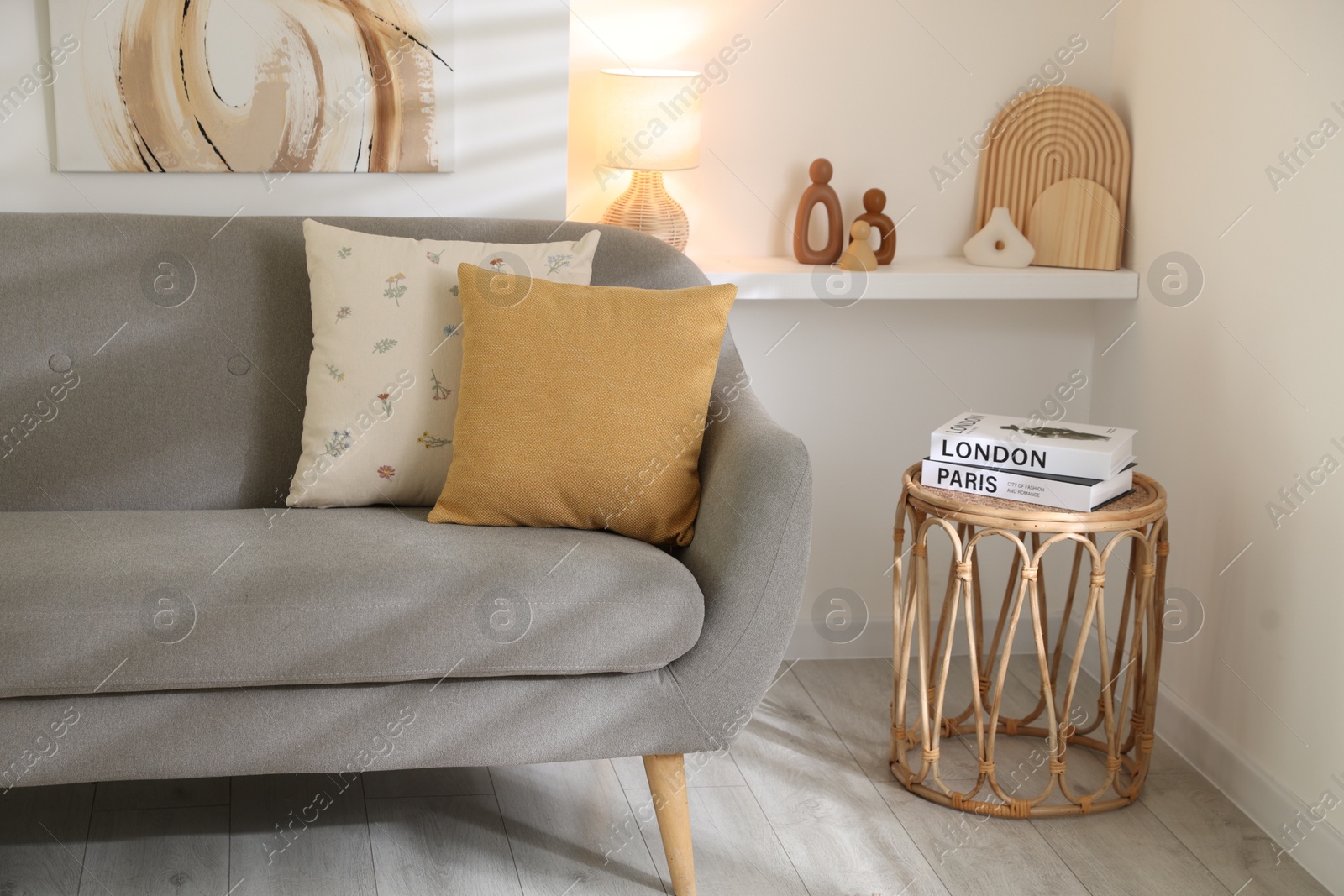 Photo of Different soft pillows on gray sofa and side table with books in living room