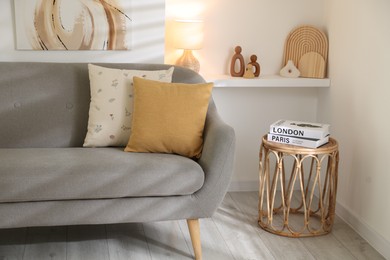 Different soft pillows on gray sofa and side table with books in living room