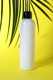 Shampoo in bottle and green palm leaves on yellow background. Personal care product