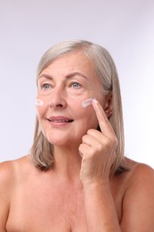 Senior woman applying face cream on white background