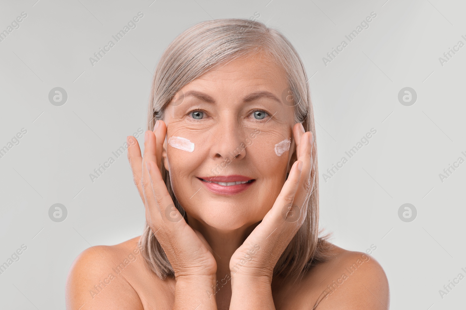 Photo of Senior woman with face cream on white background