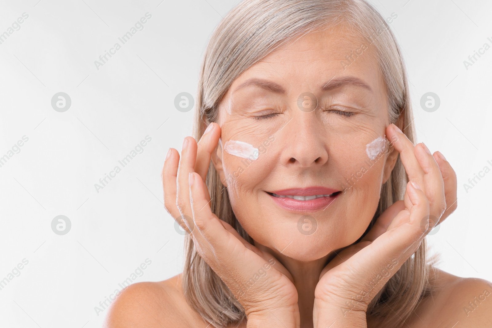 Photo of Senior woman with face cream on white background