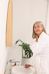 Photo of Senior woman applying face cream near mirror at home