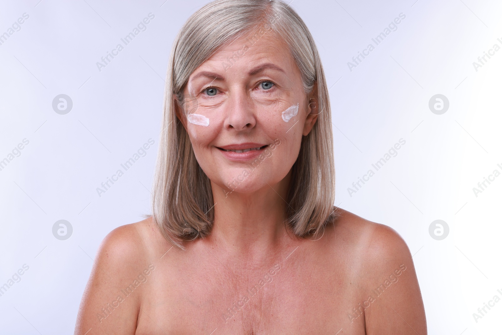 Photo of Senior woman with face cream on white background