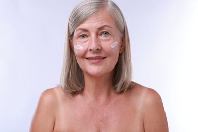 Senior woman with face cream on white background