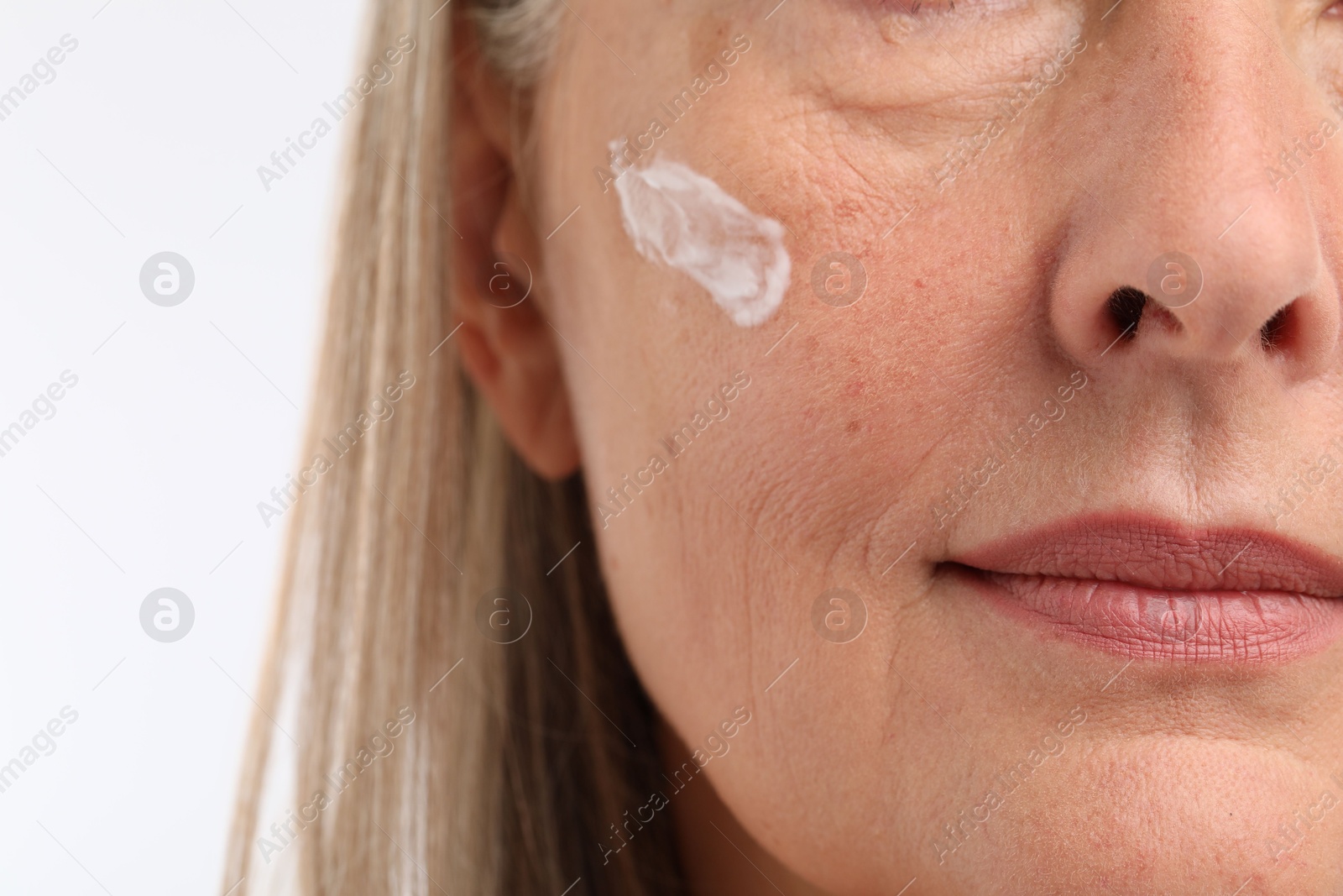 Photo of Senior woman with face cream on white background, closeup