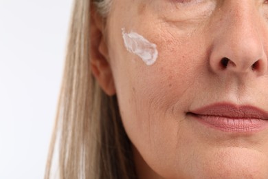 Senior woman with face cream on white background, closeup