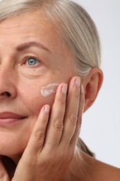 Photo of Senior woman with face cream on white background, closeup