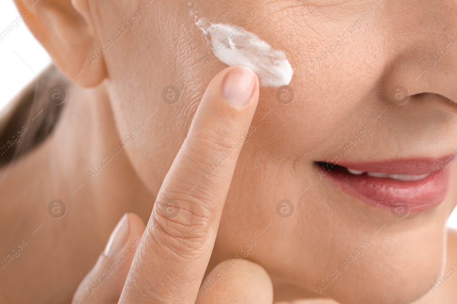 Photo of Senior woman applying face cream on white background, closeup