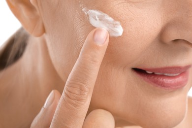 Senior woman applying face cream on white background, closeup