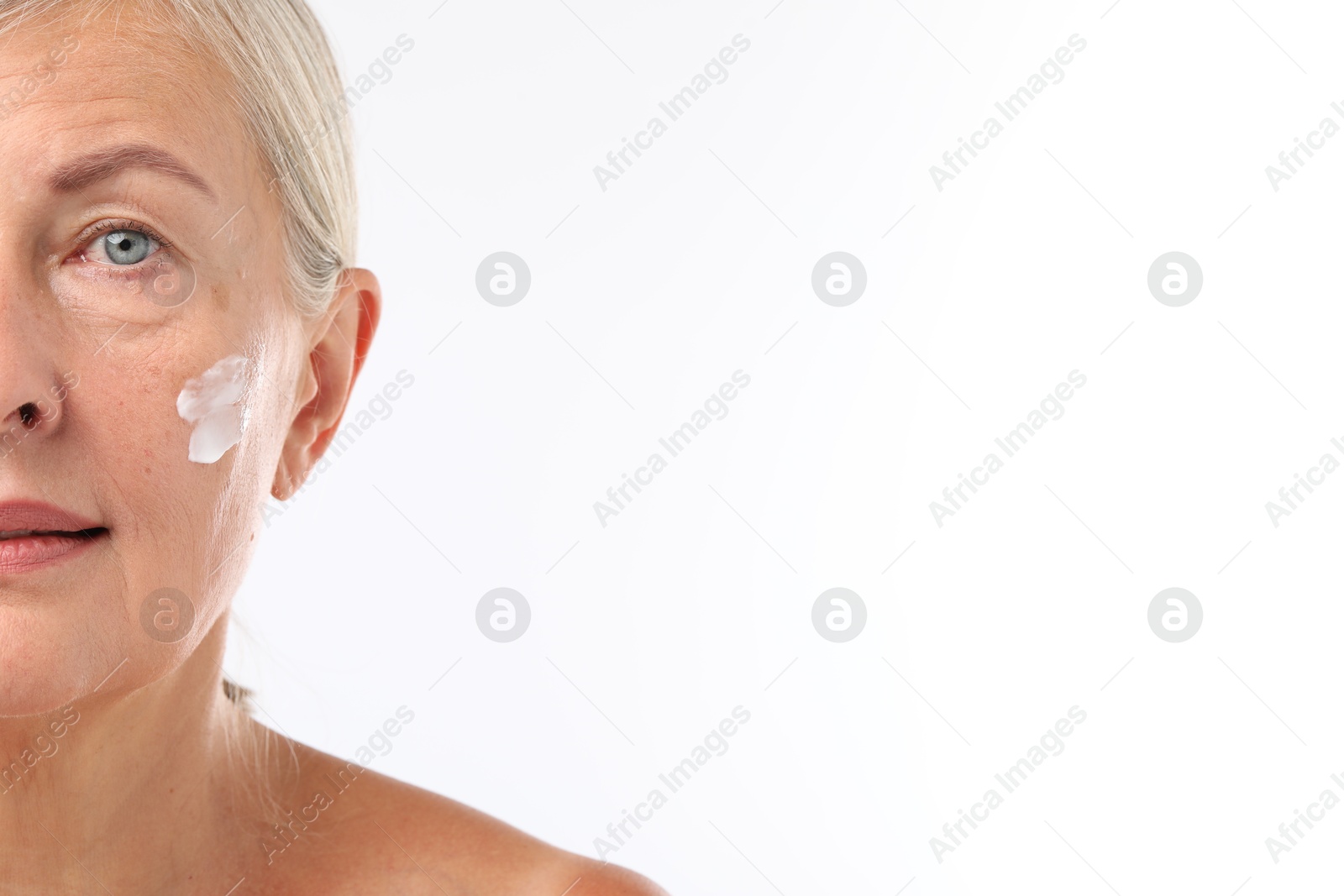 Photo of Senior woman with face cream on white background, closeup. Space for text