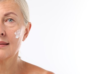 Senior woman with face cream on white background, closeup. Space for text