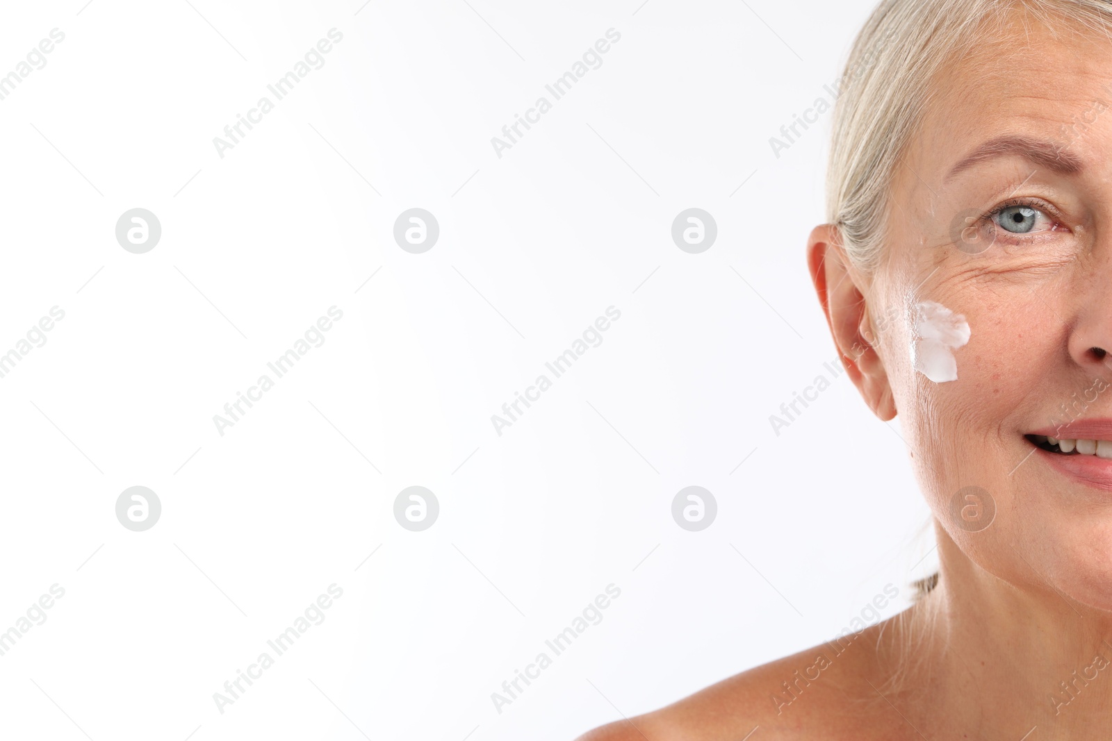 Photo of Senior woman with face cream on white background, closeup. Space for text