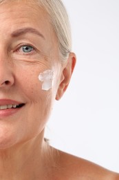 Photo of Senior woman with face cream on white background, closeup