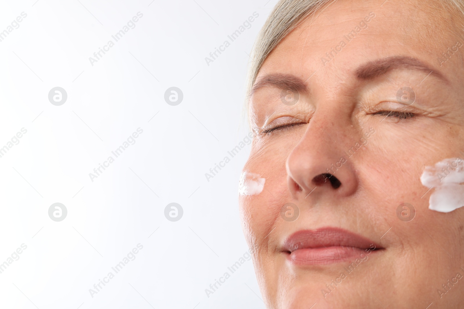 Photo of Senior woman with face cream on white background, closeup. Space for text