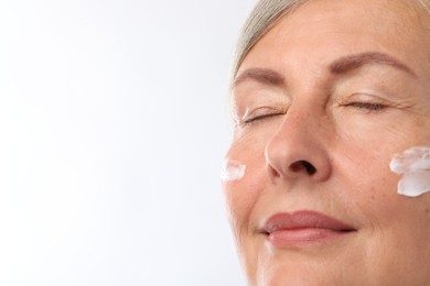 Senior woman with face cream on white background, closeup. Space for text