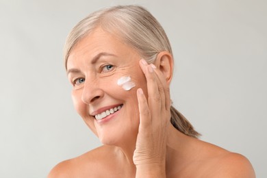 Senior woman with face cream on light background