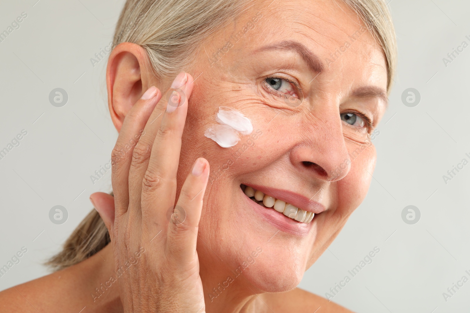 Photo of Senior woman with face cream on light background, closeup