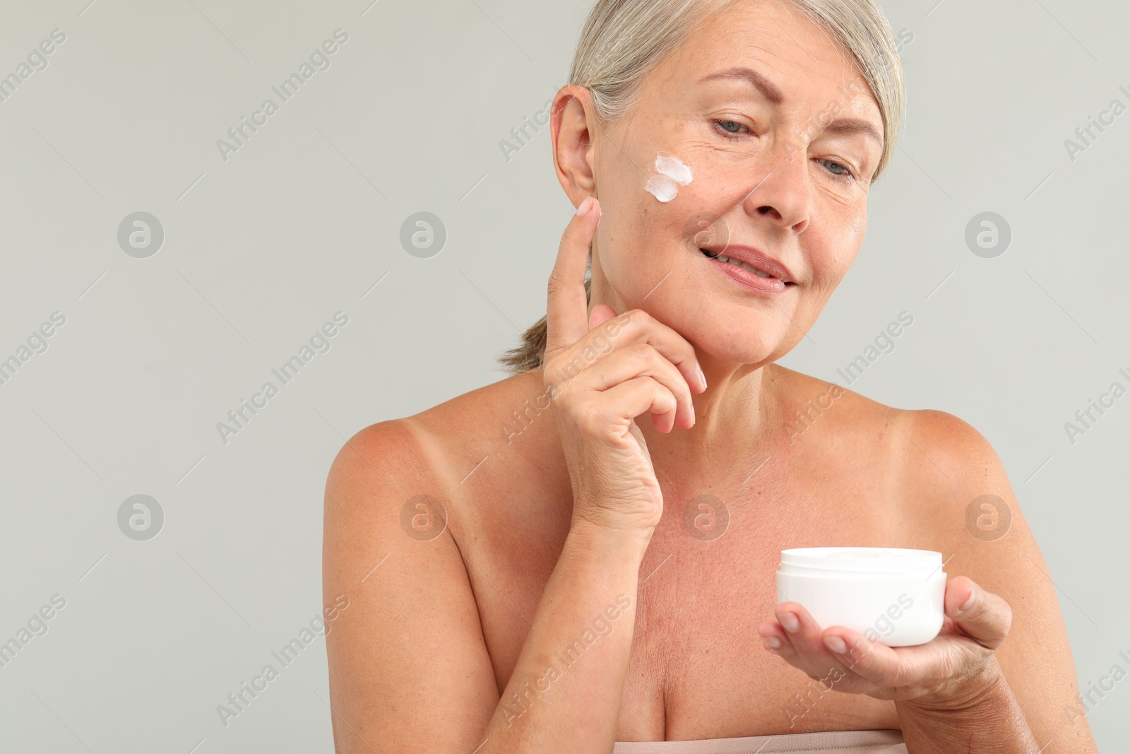 Photo of Senior woman applying face cream on light background