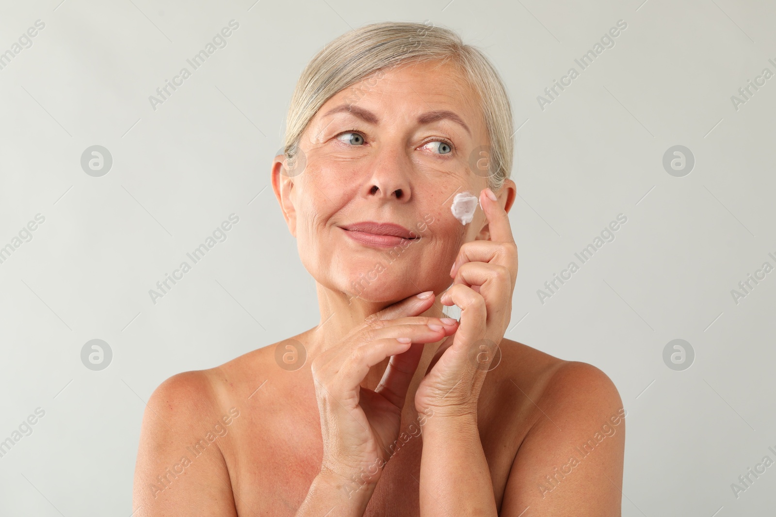 Photo of Senior woman applying face cream on light background