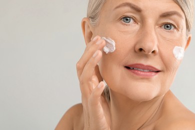 Photo of Senior woman applying face cream on light background, closeup. Space for text