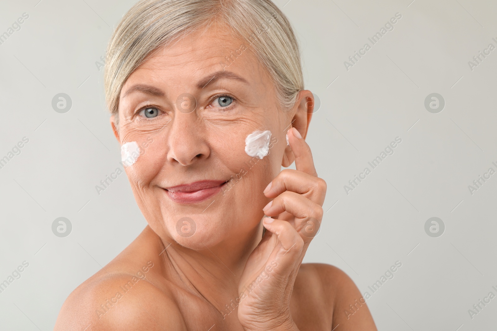 Photo of Senior woman applying face cream on light background