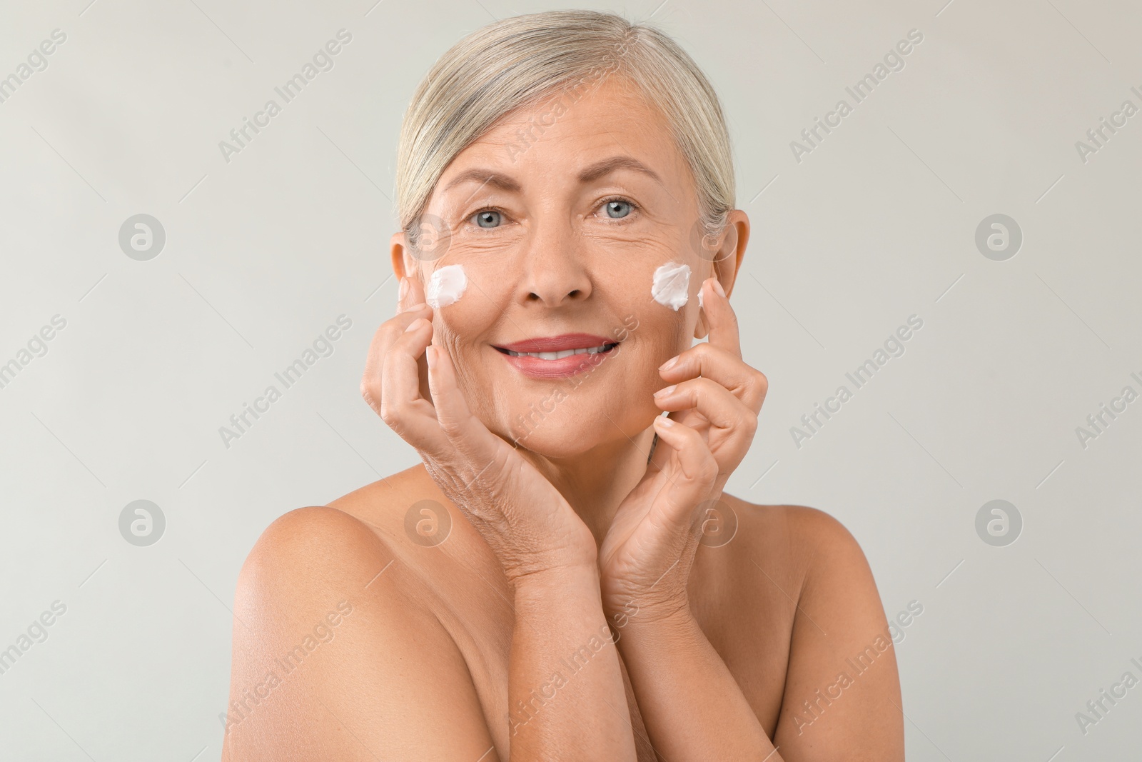 Photo of Senior woman with face cream on light background